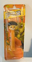 Pezz dispenser featuring Puss in Boots character in orange plastic with original Shrek 2 packaging showing character eyes behind dispenser.