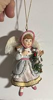 Porcelain angel ornament dressed in turn of the century style clothing, held by hand for scale, showing bonnet, wings, and detailed dress