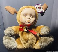 Photo of vintage Show Stoppers Babes in the Wild plush toy dressed as a deer, showing porcelain face, ears, red ribbon, bell, and attached tag.