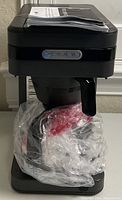 Front and top view of the black BUNN Speed Brew Elite coffee maker with carafe wrapped in protective plastic.