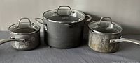 Photo of three Calphalon Classic sauce pans with lids, showing used condition and different sizes.