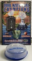 Poster celebrating Florida Gators Football and Basketball 2006 Dual National Championships with trophies and year noted, displayed behind a serving platter.