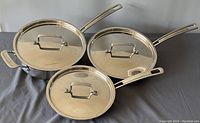 Set of three stainless steel pans with matching lids, two frying pans and one sauce pan