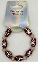 Photo of a handmade football themed beaded bracelet on display card labeled 'Handmade with love'. Bracelet consists of brown football-shaped beads and beige round beads.