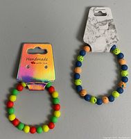 Two neon multicolor beaded elastic bracelets on display cards, one with holographic card and one with marble card, showing bead colors and arrangement.