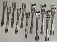Photo shows 12 stainless steel forks laid out, 6 with decorated handles (Reppel Inox 18/8) and 6 with plain handles (Cambridge). All have three tines.