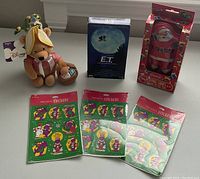 Photo showing Disney Pooh plush with tags, three Barney Hallmark sticker packs, Coca Cola playing card set in Santa tin, and E.T. VHS tape