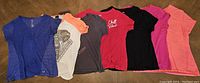 Seven women's large plus size shirts in various colors laid out flat.