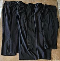 Five pairs of black women's plus size pants laid on a floor, showing full length and variety in style.
