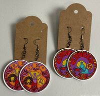 Two pairs of round multicolor zodiac sign dangle earrings with hooks on brown display cards