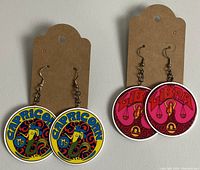 Two pairs of new zodiac-themed dangle earrings on tags, one Capricorn design in blue/yellow, one Libra design in pink/red.