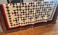 Full view of one handmade quilt with dark purple, white, and red geometric patchwork displayed over a wooden surface