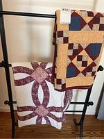 Two quilts draped on black metal quilt rack on hardwood floor