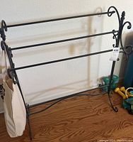 Full view of one black metal quilt rack with scrollwork and three horizontal bars for quilt hanging.