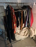 Photo showing one metal rolling clothing rack filled with various clothing items such as sweaters, jackets, and pants.