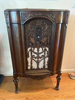 Full front view of the antique console radio showing detailed wood carving, fabric speaker cover, and carved legs.