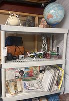 Shelf with Canon camera, lenses, model airplane, decorative figurines, books and magazines.