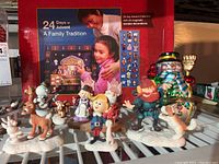 Photo showing several nativity and holiday figurines arranged in front of the Magnetic Nativity Advent Calendar boxed set, featuring deer, snowmen, and elf characters.