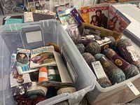 Plastic bin with skeins of multicolored yarn, crochet and knitting tutorial booklets, and tools.