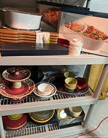 Overview photo showing the Corningware boxed baking dish, Cutco knife case, wooden cutting boards, ceramic container, and assorted ceramic dishes on a plastic shelving unit.