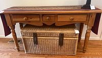 Full view of the console table from front, showing three drawers and a wicker chest underneath.