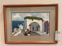 Watercolor painting of Greek-style white buildings overlooking the sea, framed in carved wood-tone frame with gray mat