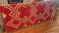 Full view of handmade red quilt draped over railing showing overall pattern and color.