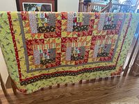 Photo of two handmade patchwork quilts draped over a wooden railing, showing colorful fabric patterns with monkeys, bananas, and geometric shapes.
