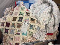 Patchwork quilted pillow displaying various fabric prints with cream lattice work and a crocheted pastel blanket alongside folded quilts beneath.
