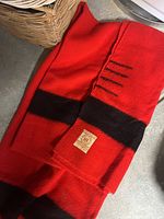 Red wool blanket with black stripes folded showing label with Hudson's Bay Company seal.