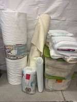 Photo of rolled white cotton batting labeled Warm & White and fiber fill packages stacked with fabric rolls and storage containers.