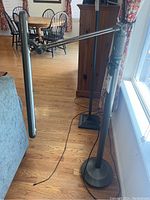 Black OttLite floor lamp with adjustable arm positioned near a window and wooden floor. Lamp has a rectangular light panel extending horizontally.