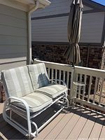 Wide view of patio glider with white metal frame and striped cushions, showing side profile and umbrella next to it