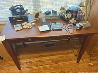 Full view of wooden desk with items including wired headset, wireless charger, calculator, pens, stapler, lamp, alarm clock, and tablet with accessories