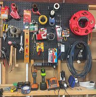 Overall pegboard workspace with assortment of tools, tapes, drills, and hardware.