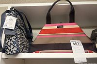 Two handbags on shelf, a blue and white Nike bag with tags and a Kate Spade multicolor striped canvas bag