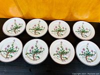 Eight round ceramic plates arranged on table, showing botanical illustration of 'Thymus pulegioides' plant and brown rim