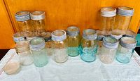 Front view of all jars showing various sizes and two-tone glass color (clear and blue-tinted), with metal lids on most jars.