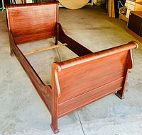 Full view of the antique mahogany twin sized sleigh bed frame showing headboard, footboard and side rails on a concrete floor.