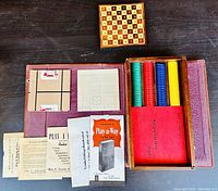 Top-down view of the open game box showing playing cards, paper score sheets, instruction booklets, colored poker chips, and the small chess/checkers board.