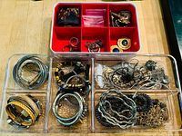 Overview of jewelry pieces in red and clear trays including bracelets, rings, and silver items