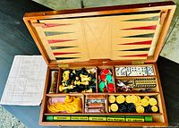Open view of the wooden box with multi-game compartments showing backgammon board, chess and checkers pieces, domino tiles, colorful chips, horse figurines and multiple game boards.