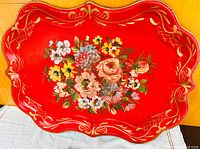 Top view of red metal toleware tray showing floral hand painted bouquet and gold decorative border on scalloped edges.