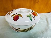 Round white porcelain lidded dish with painted plum and peach fruit decoration on lid.