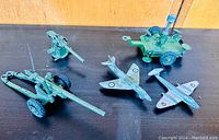 Four vintage Dinky Toys military models including 2 gunners, 2 aircraft, and a missile erector on wooden surface.