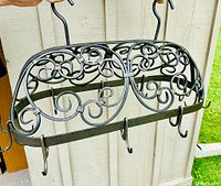 Front view of black wrought iron hanging pot rack with decorative scrollwork and 3 hooks visible in the front row
