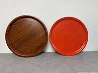 Photo showing front view of the two circular wooden trays side-by-side, teak on left and red lacquer on right.