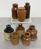 Front view of eight antique English stoneware bottles with a variety of brown shades and shapes.