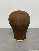 Front view of antique millinery hat display head mannequin showing brown fabric with vertical stitching and white fabric trim at bottom.