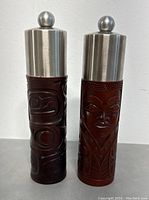 Front view of two carved totem pole salt and pepper grinders with silver tops.